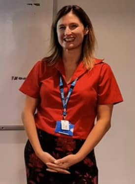 Profile shot of Kristy Atkinson. Women standing smiling at camera, she is dressed smart wearing a lanyard.