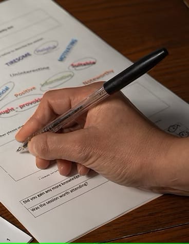 Image of a hand holding a pen and writing onto a document. The document has many words printed onto it.